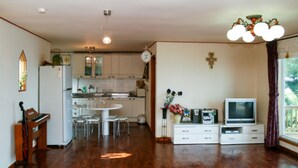 A spacious living area with a wooden floor, a dining table, a kitchen with white cabinets, a television, and a clock on the wall. - Badasol Fragrance Pension (Taean)