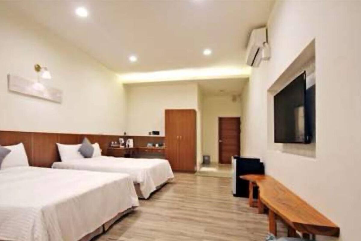 Habitación de hotel con dos camas, cabecero de madera, televisor de pantalla plana montado en la pared y un banco de madera.