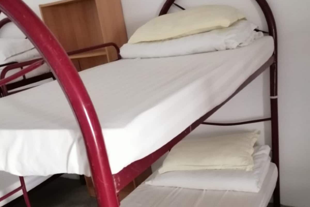 Een stapelbed met een houten hoofdbord, witte beddengoed en een klein houten plankje.
