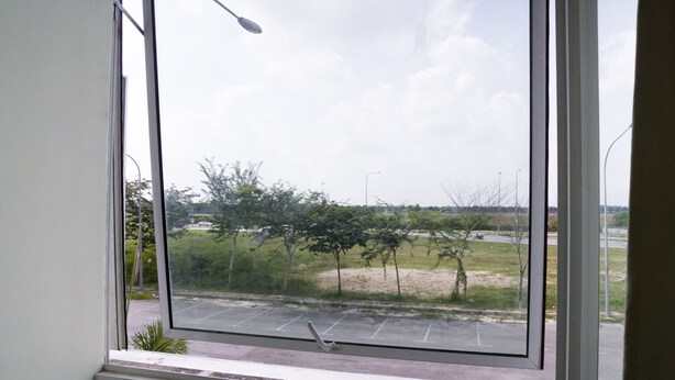 A view through a window of a parking lot and a grassy area with trees. - Hotel O Sohotel (Pelabuhan Klang)