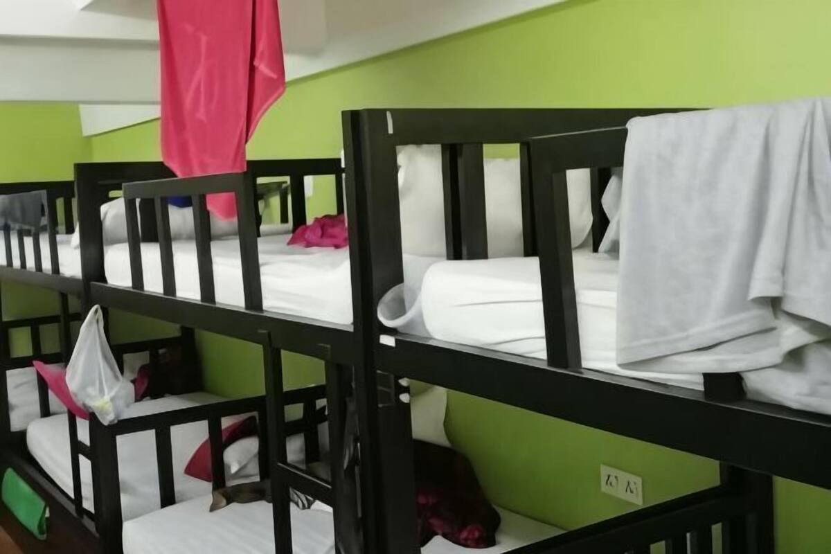 Tweepersoonsbed met witte lakens, een groene muur en een zichtbaar stopcontact.