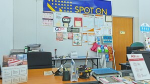 A hotel reception desk with various informational posters, a POS Laju sign, and a 'Spot On' banner. - Hotel O Sohotel (Pelabuhan Klang)