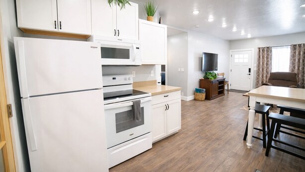 A modern kitchen with white cabinetry, a built-in microwave, and an oven. There is a dining area with a table and chairs.