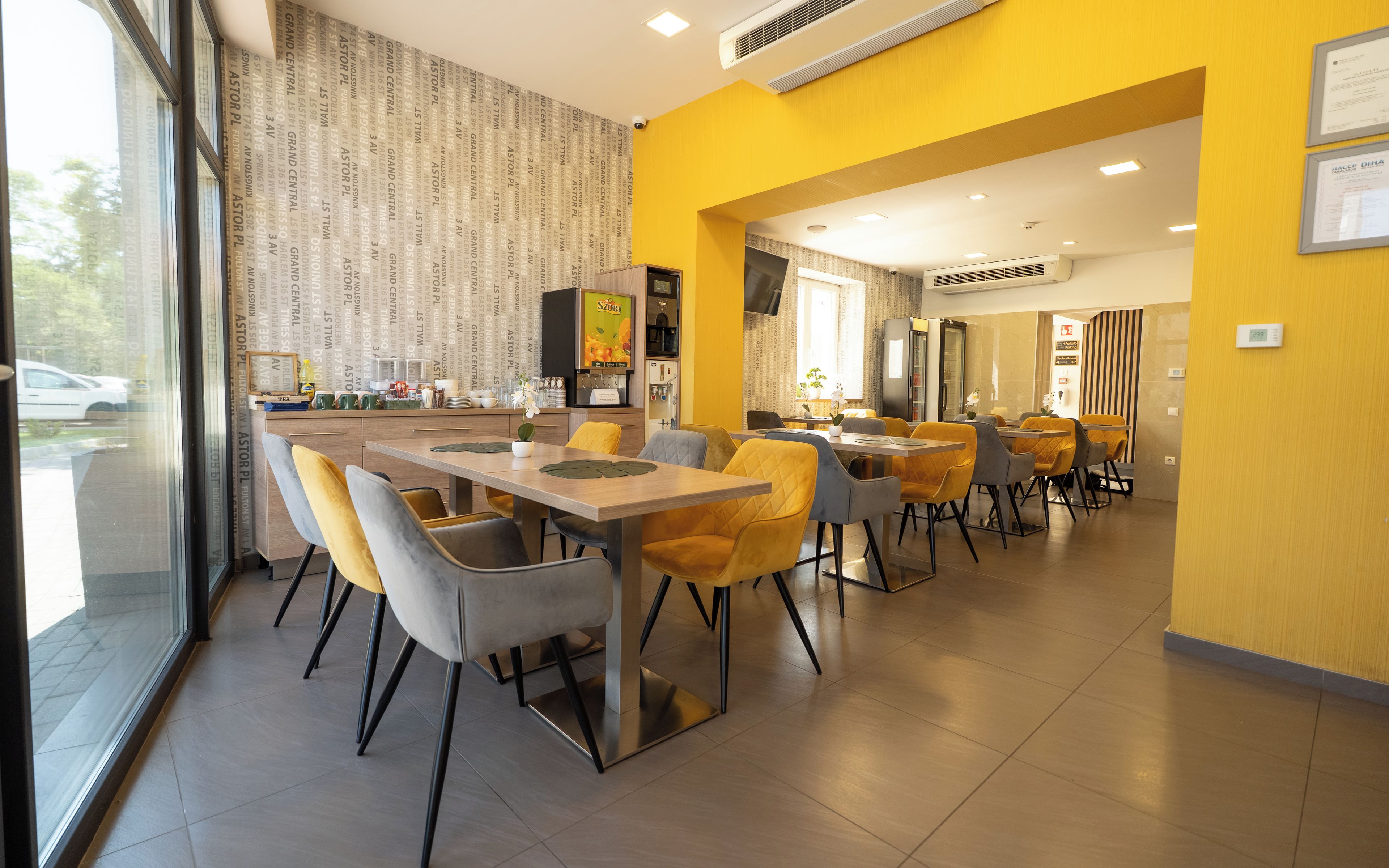 Un comedor moderno con mesas y sillas, una zona de cocina y vistas a través del ventanal.