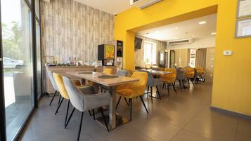 Un comedor moderno con mesas y sillas, una zona de cocina y vistas a través del ventanal.