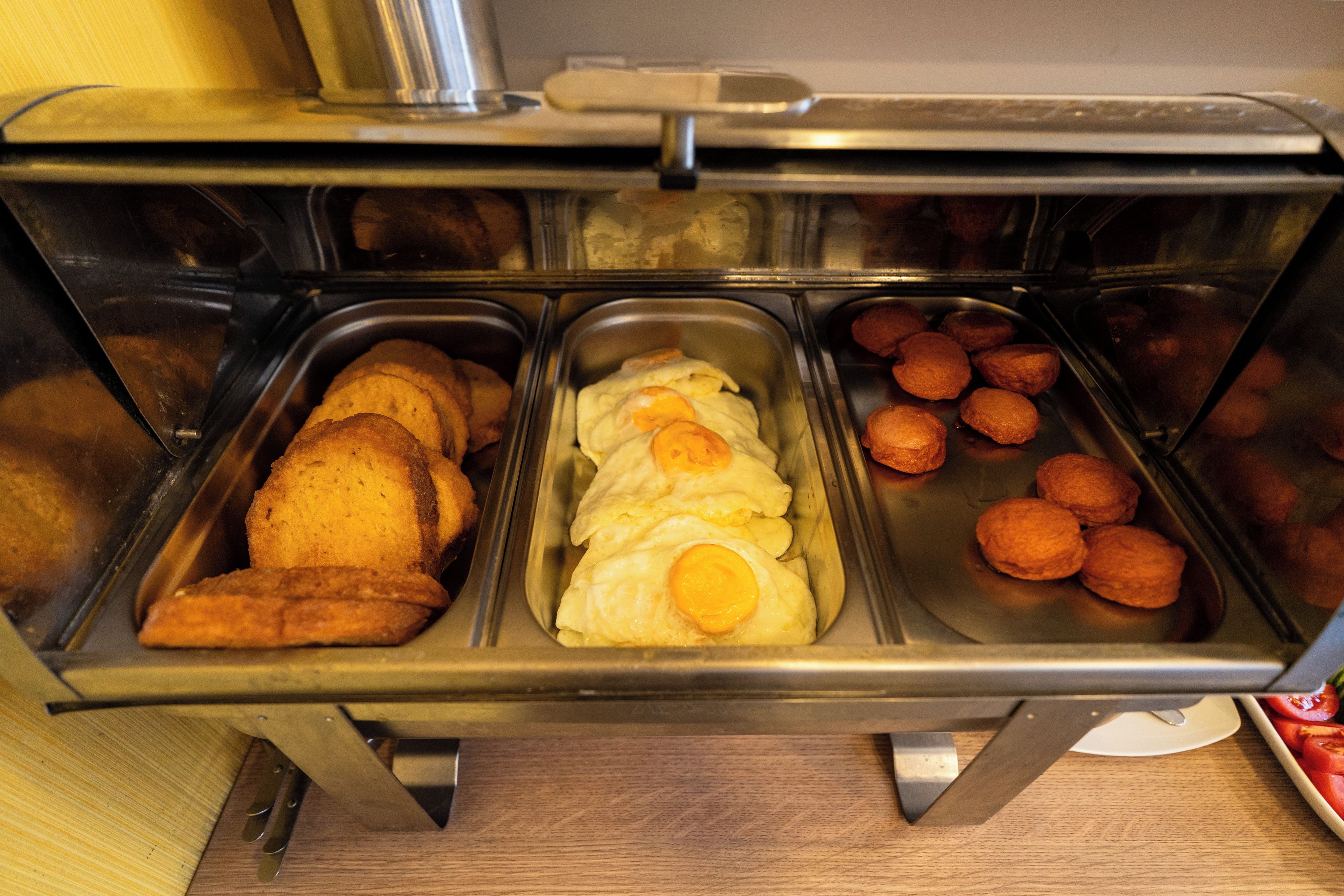 A buffet with various food items including bread, eggs, and meat.