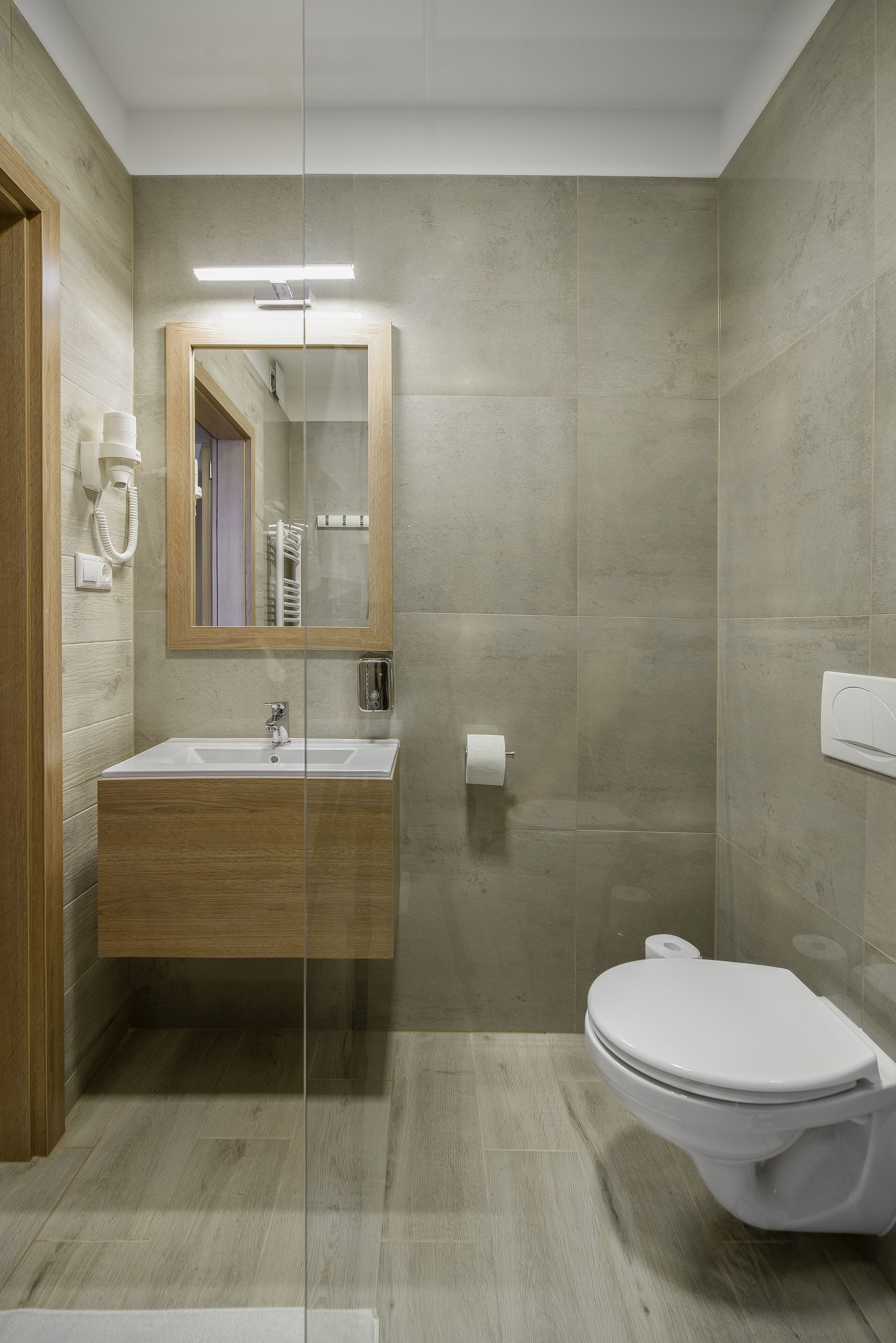 A modern bathroom with a wooden vanity, a glass shower enclosure, and a toilet.
