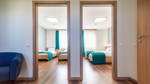 A hotel room with two beds, a blue chair, and a wooden floor. - Hotel Szeghalom (Szeghalom)