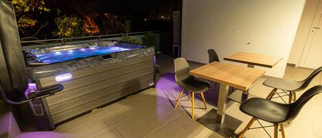 Un área de jacuzzi exterior con una mesa y sillas de madera, rodeada por un patio de baldosas.
