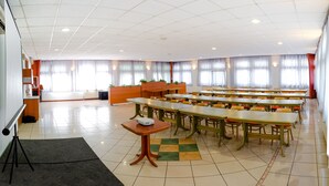 A spacious conference room with multiple tables and chairs, a podium, and a projector on a table. - Hotel Szeghalom (Szeghalom)