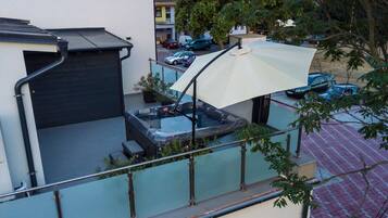 A rooftop patio with a hot tub, a covered seating area, and a view of parked cars and buildings in the background.
