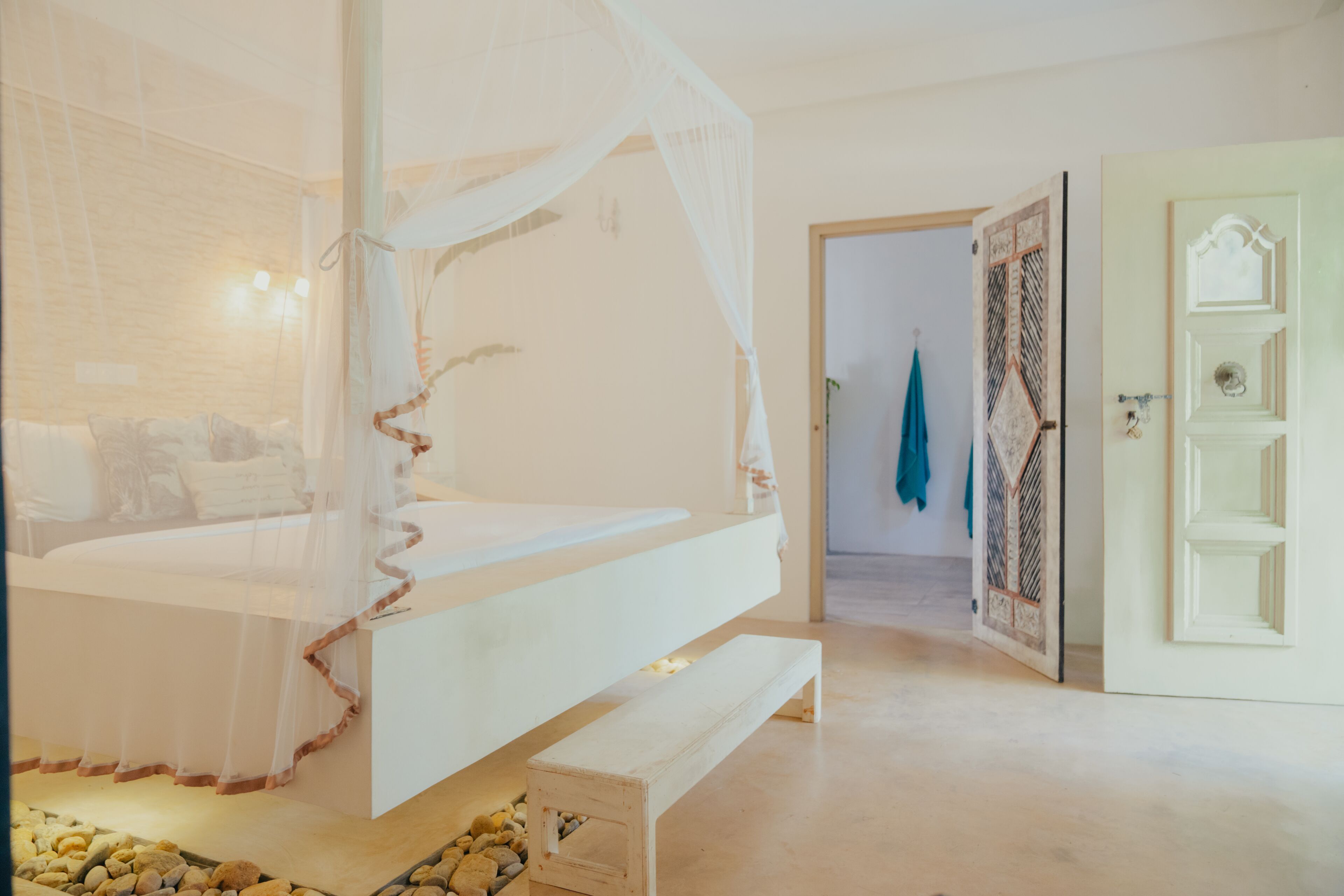 A bedroom with a canopy bed, a bench, and a door with a patterned design.