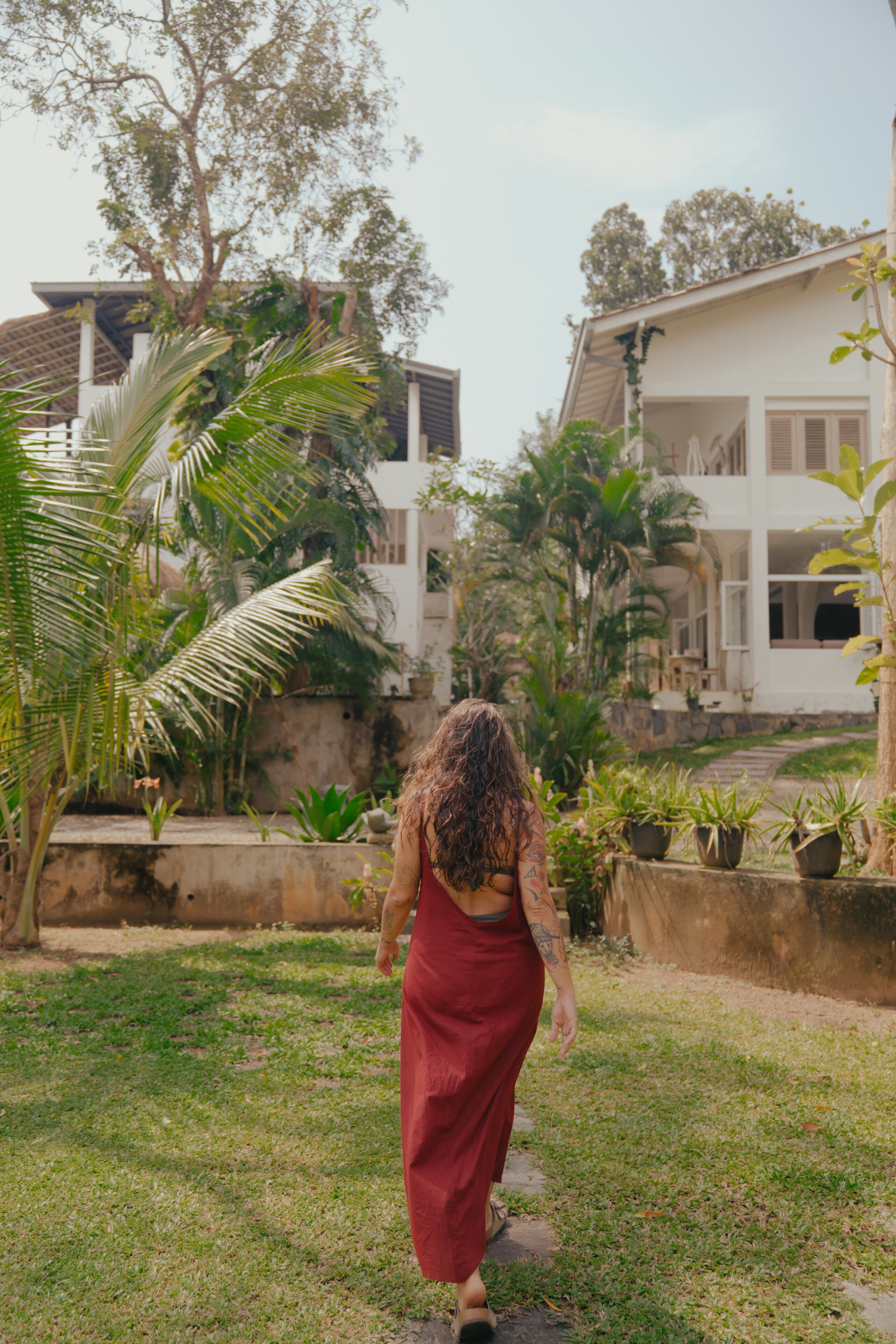 A woman walking on a path surrounded by greenery and buildings.