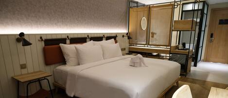 A modern hotel room with a large bed, a wooden desk, a chair, and a window with a view.
