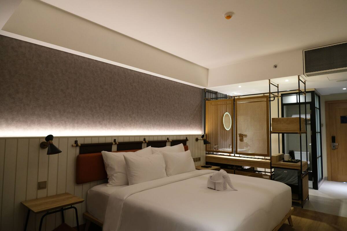 A modern hotel room with a large bed, bedside tables, a desk, and a wardrobe with a mirror.