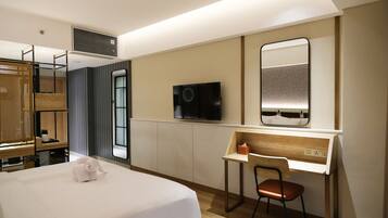 Habitación de hotel con cama, escritorio, silla, televisor y espejo.