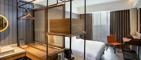 A hotel room with a bunk bed, a desk with a chair, a vanity with a mirror, and a large window with curtains.