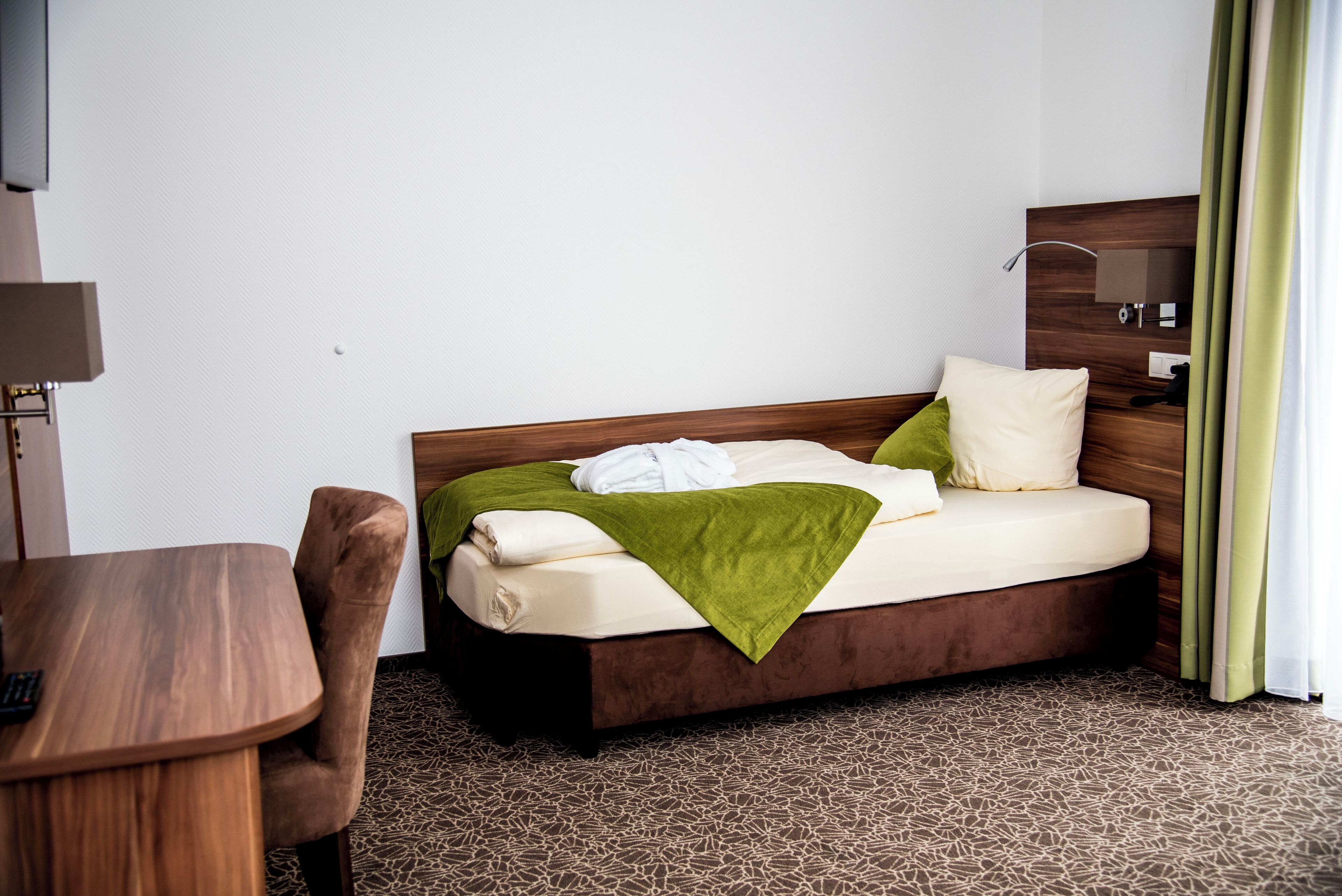 Una habitación de hotel ordenada con una cama, una mesita de madera y una silla.