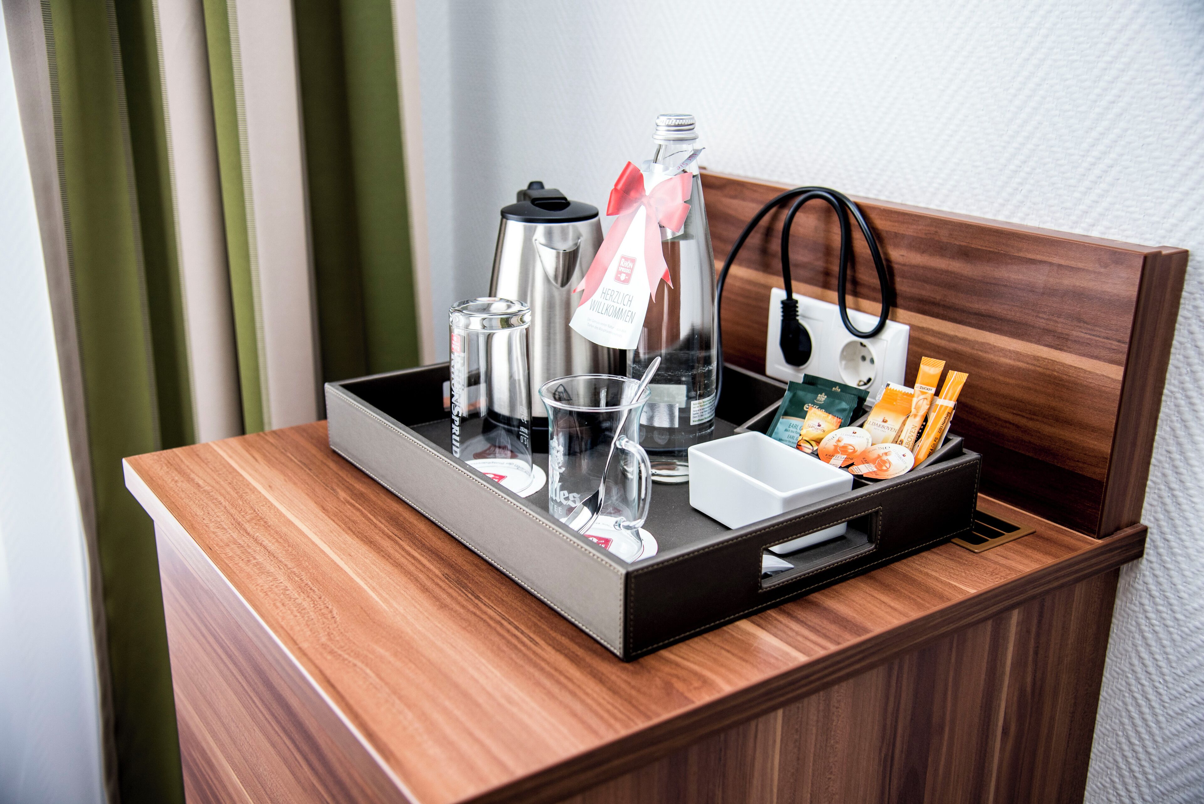 A wooden counter with a tray containing a coffee maker, a glass, a bottle, and some snacks.