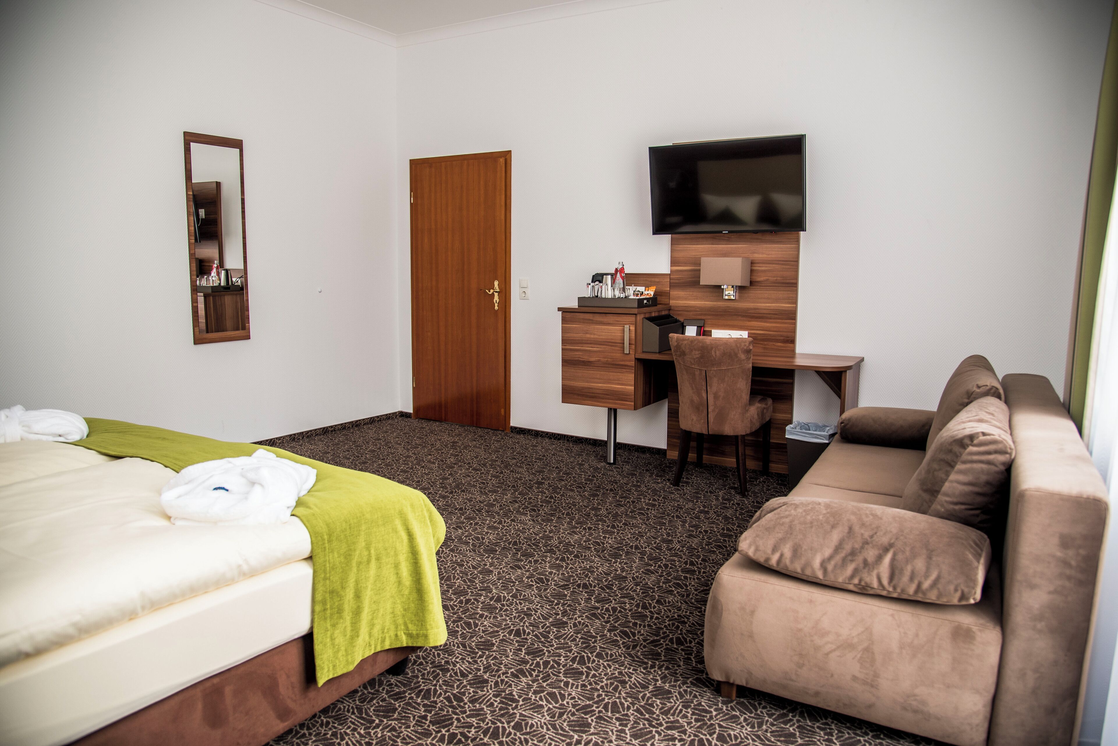 A hotel room with a bed, a desk, a television, and a sofa.