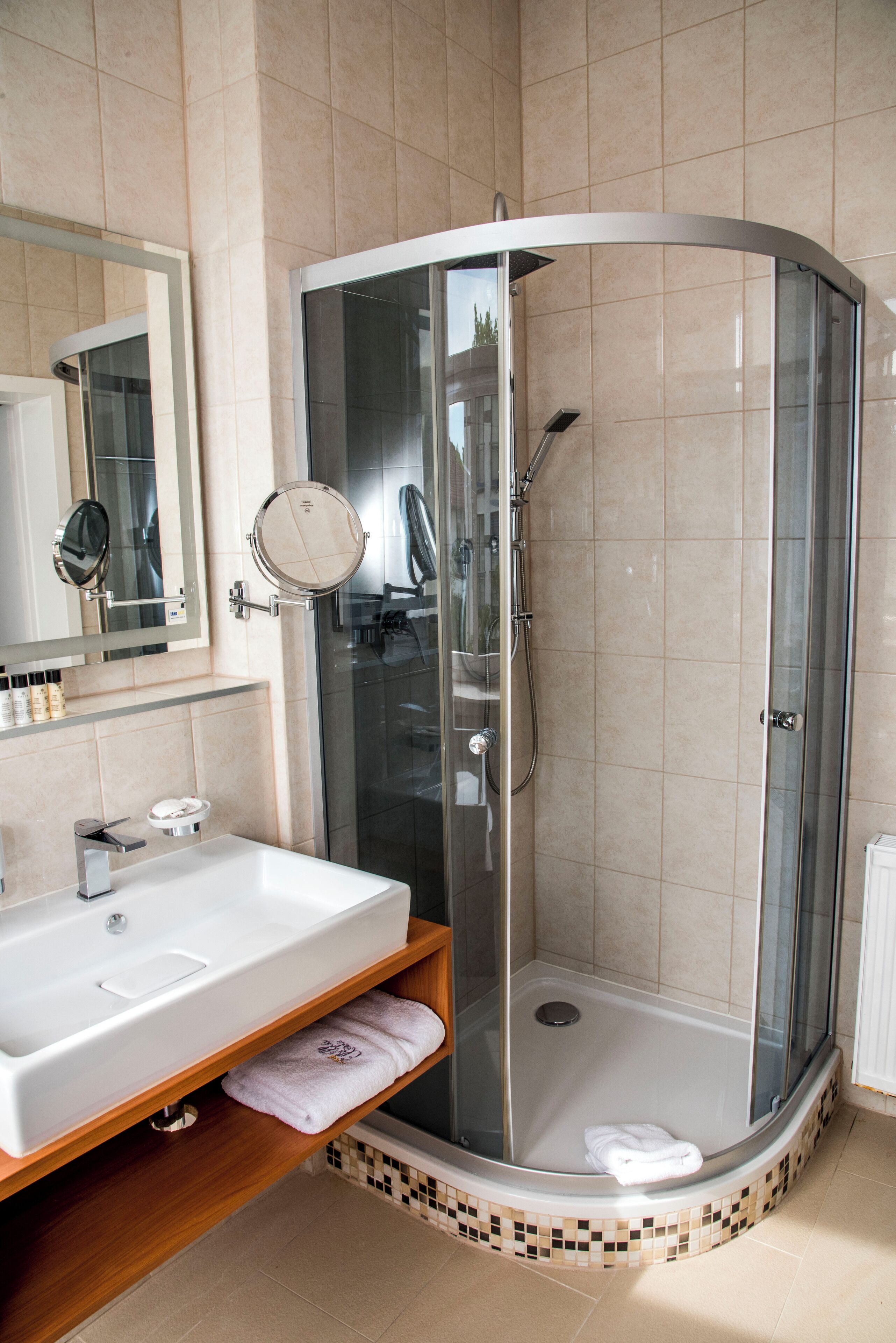 A modern bathroom with a glass-enclosed shower, a white sink, and a mirror with a round frame.