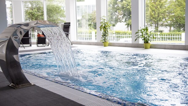 Piscina interior moderna com um elemento aquático e grandes janelas.