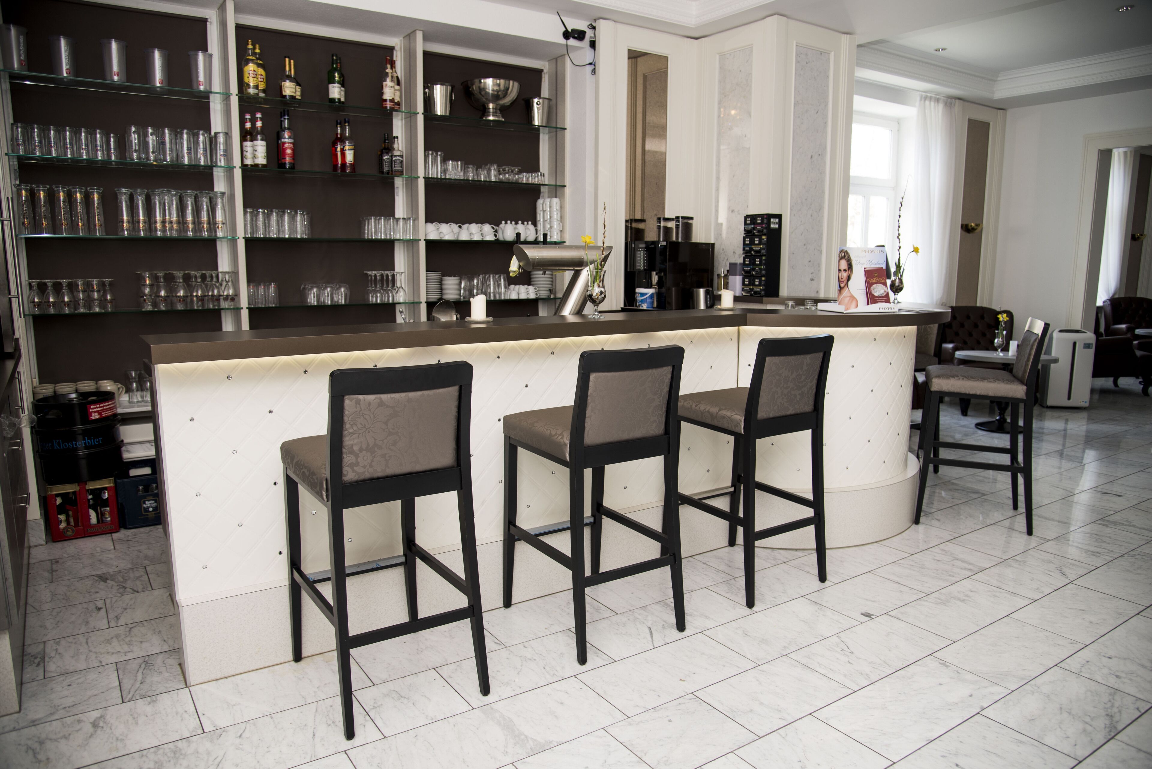 A modern kitchen with a bar area, featuring a marble countertop, bar stools, and a coffee machine.