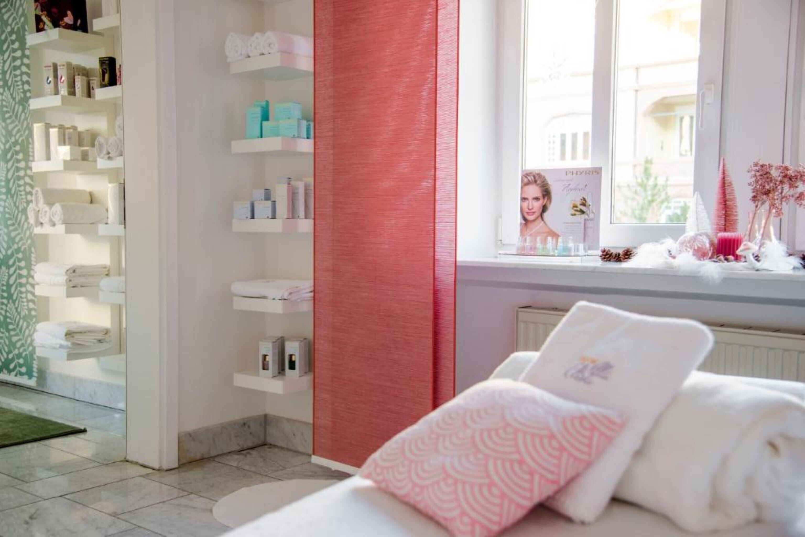 A hotel room with a bed, a window with a view, a shelf with toiletries, and a red curtain.