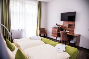 A hotel room with two beds, a desk, a chair, a TV, and a window with curtains. - Hotel Villa Elsa (Bad Kissingen)