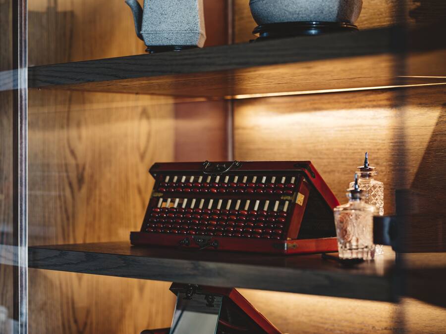 A vintage typewriter on a wooden shelf with a glass cabinet beside it.