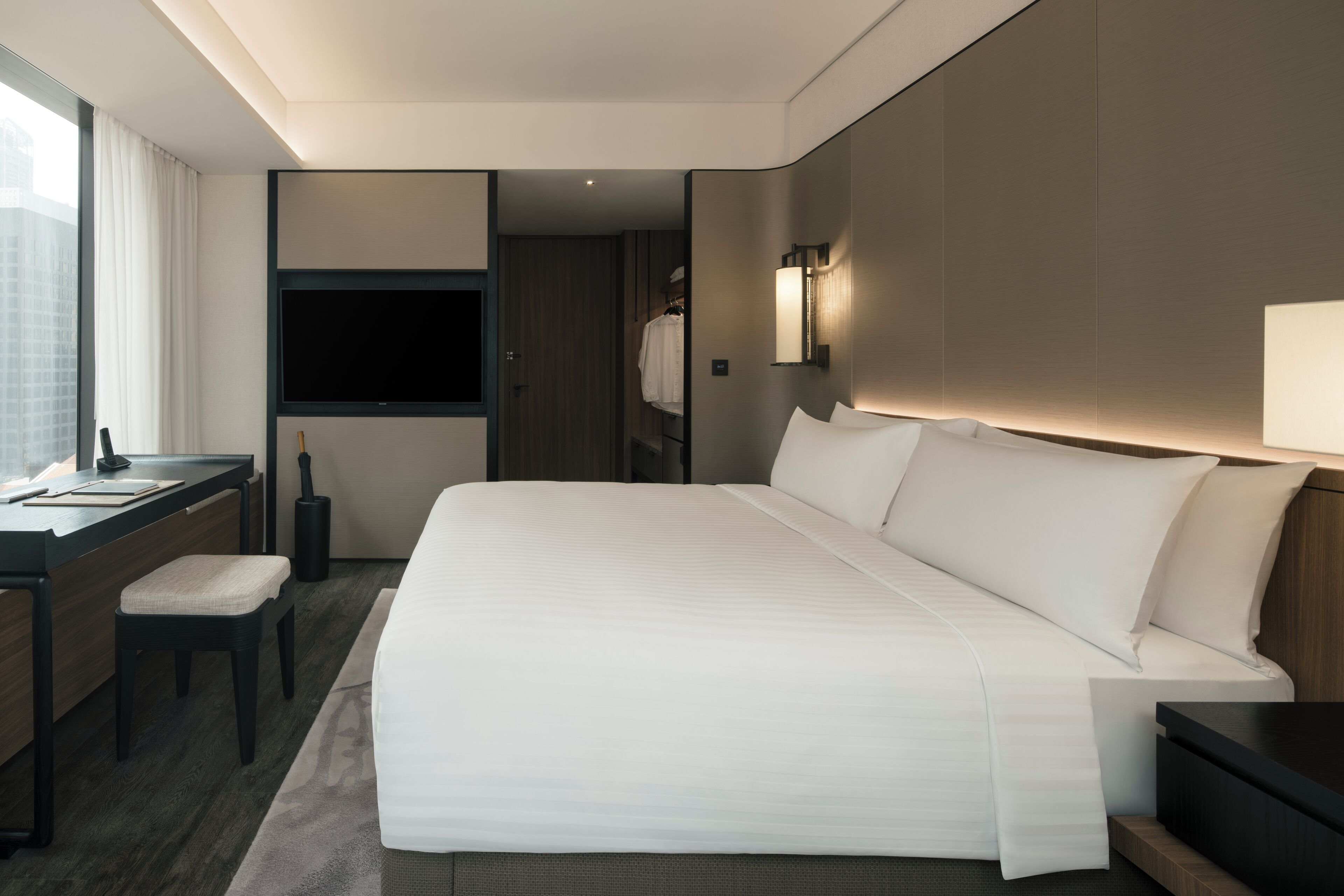 Una habitación de hotel moderna con una cama grande, un escritorio, una silla, un televisor y un armario.