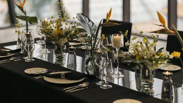A dining table set with glassware, plates, and candles, surrounded by floral arrangements.