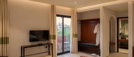 A modern hotel room with a flat-screen TV, a wooden console table, a sofa, a small table with a bowl of fruit, and a sliding door leading to a balcony.