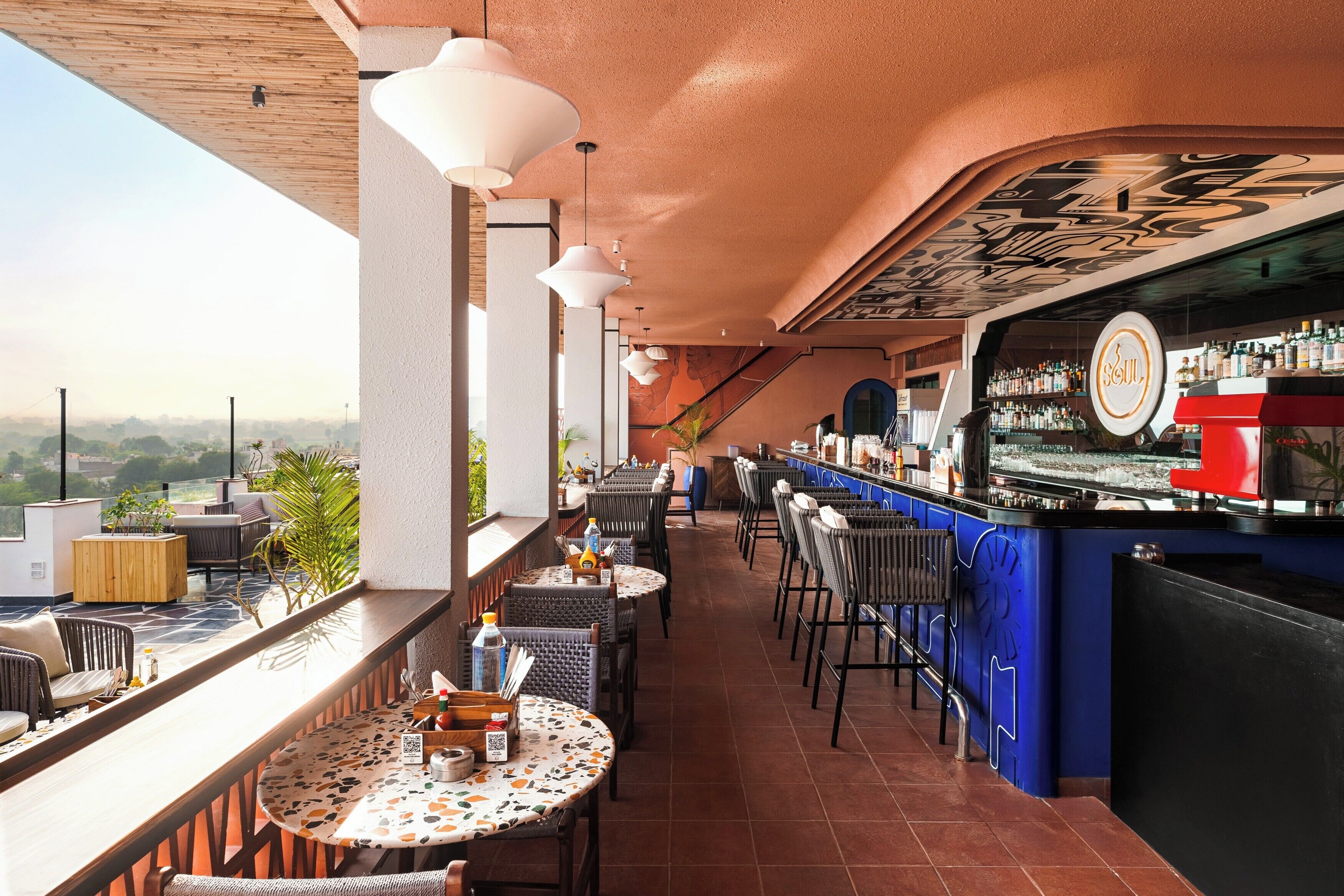 A rooftop bar with outdoor seating, a bar counter, and a view of the cityscape.