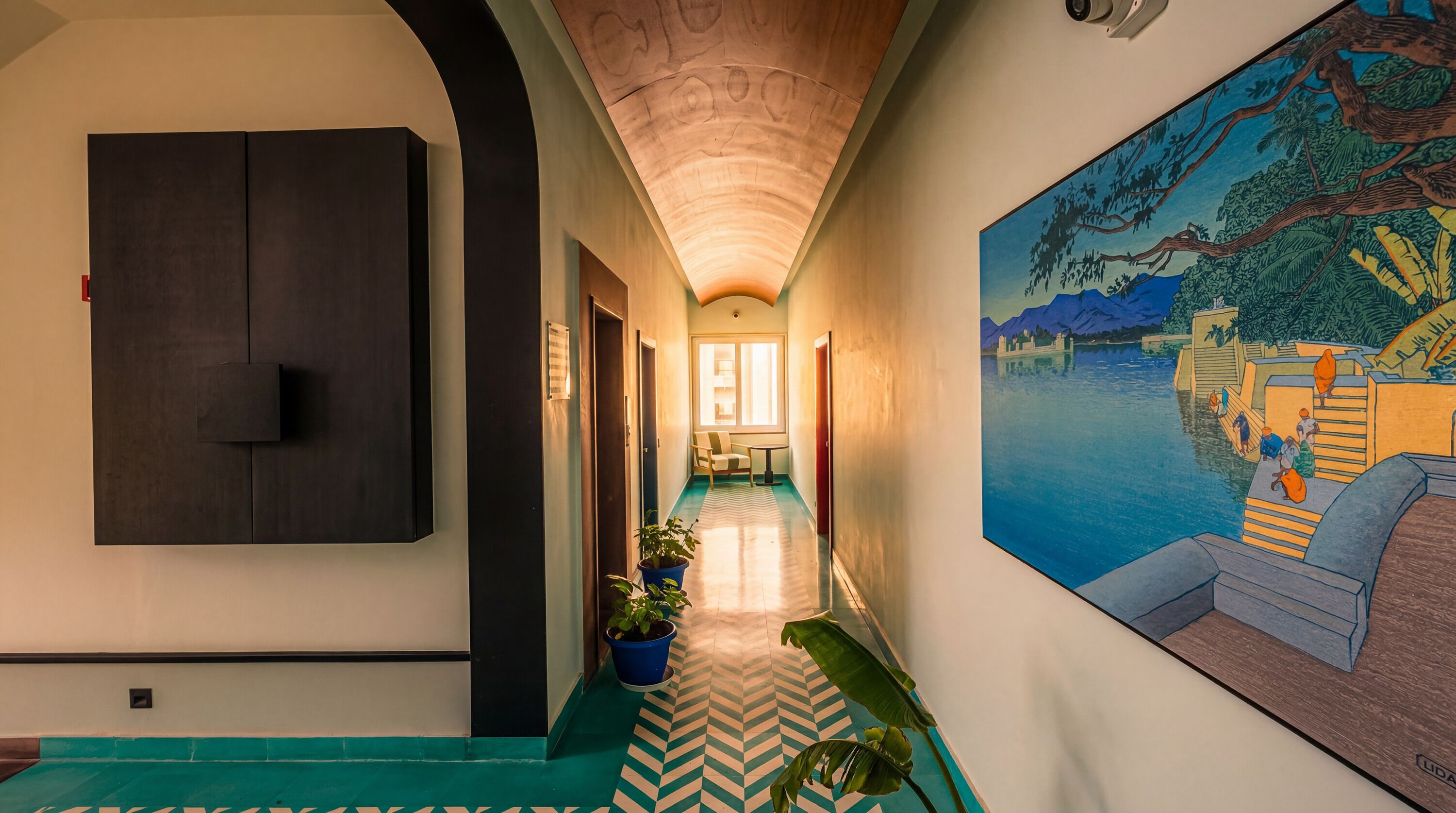 A hallway with a patterned floor, a large painting on the right, and a potted plant in the center.
