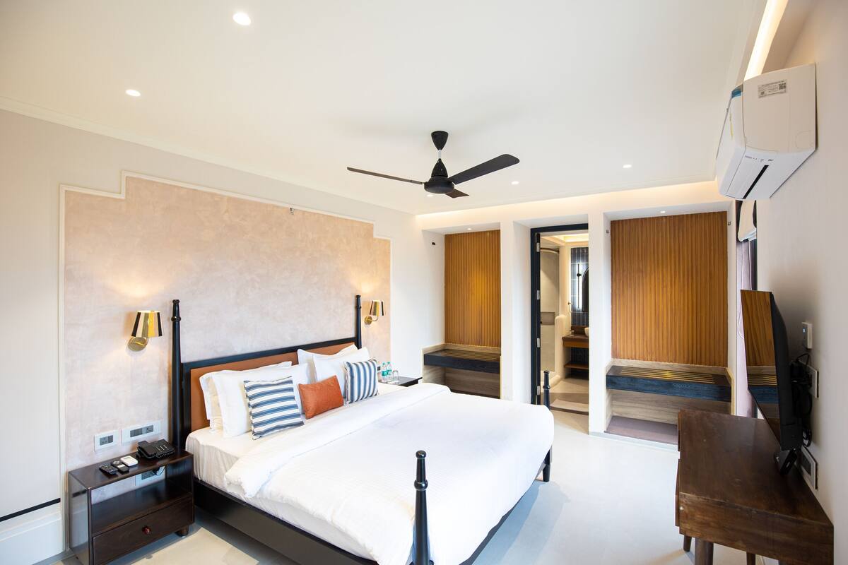 Une chambre d’hôtel moderne dotée d’un grand lit, de tables de chevet, d’un ventilateur de plafond et d’un appareil de climatisation.