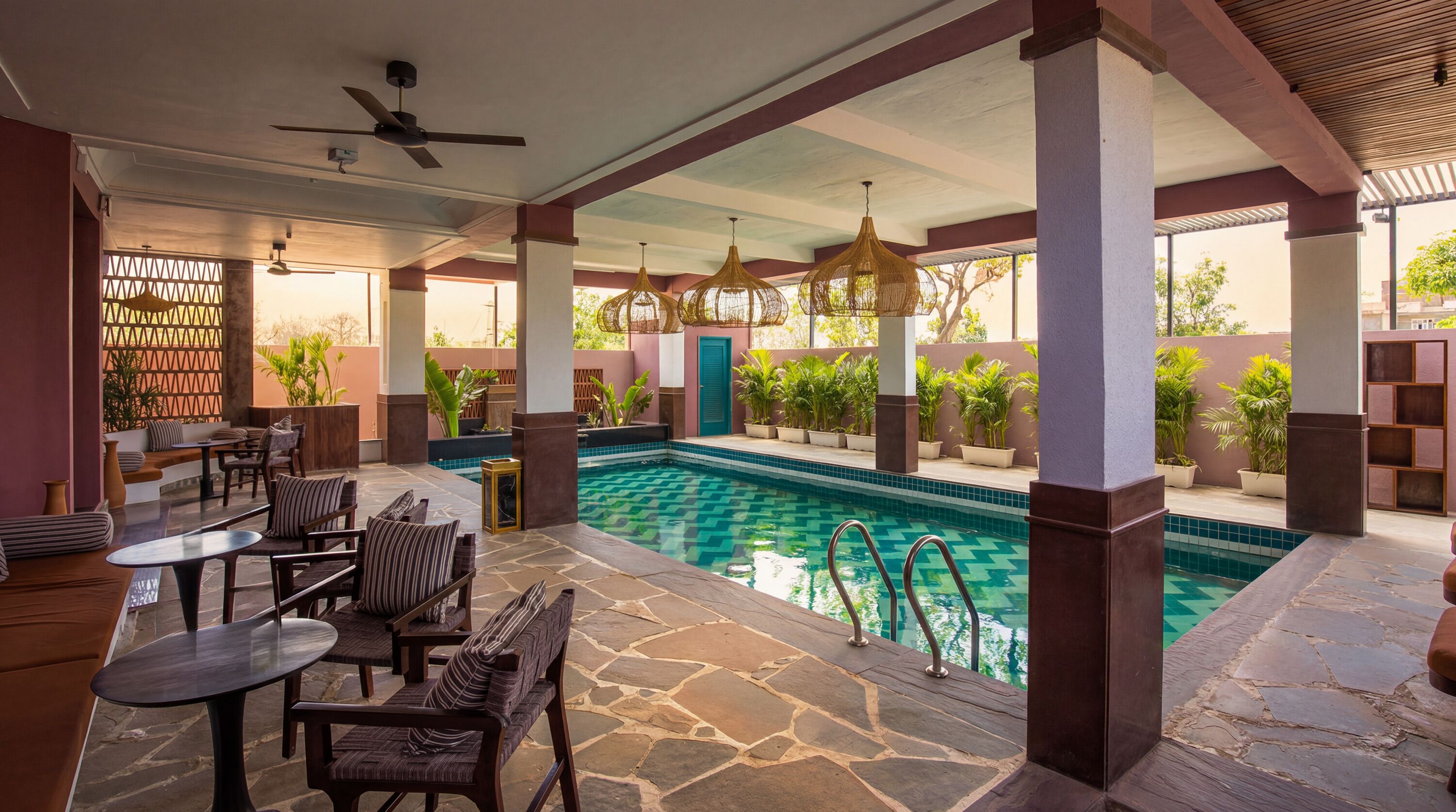 A pool area with stone flooring, lounge seating, and a ceiling fan.