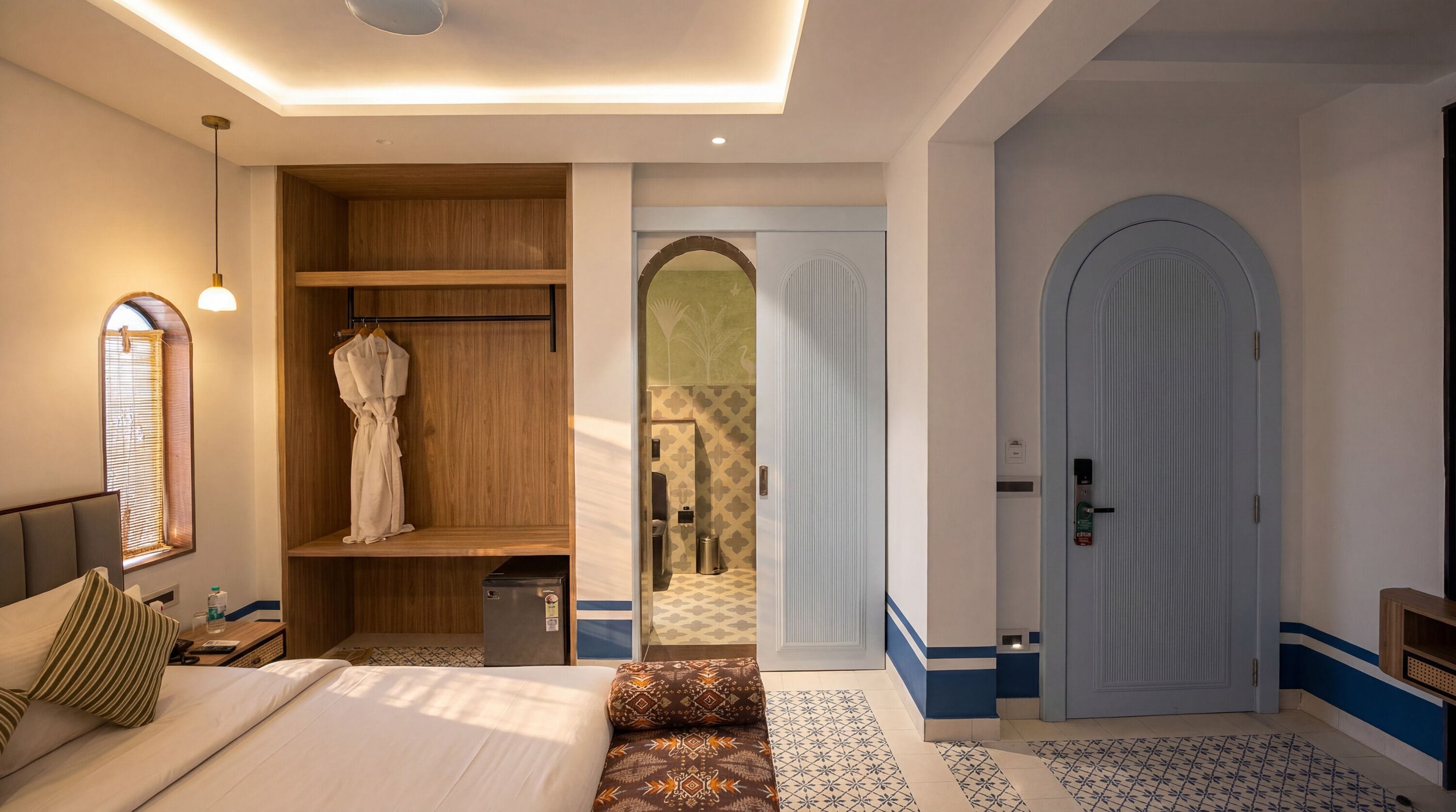 Une chambre à coucher comprenant un lit, une armoire, une petite table avec une bouteille, un banc et une porte donnant sur une salle de bain.