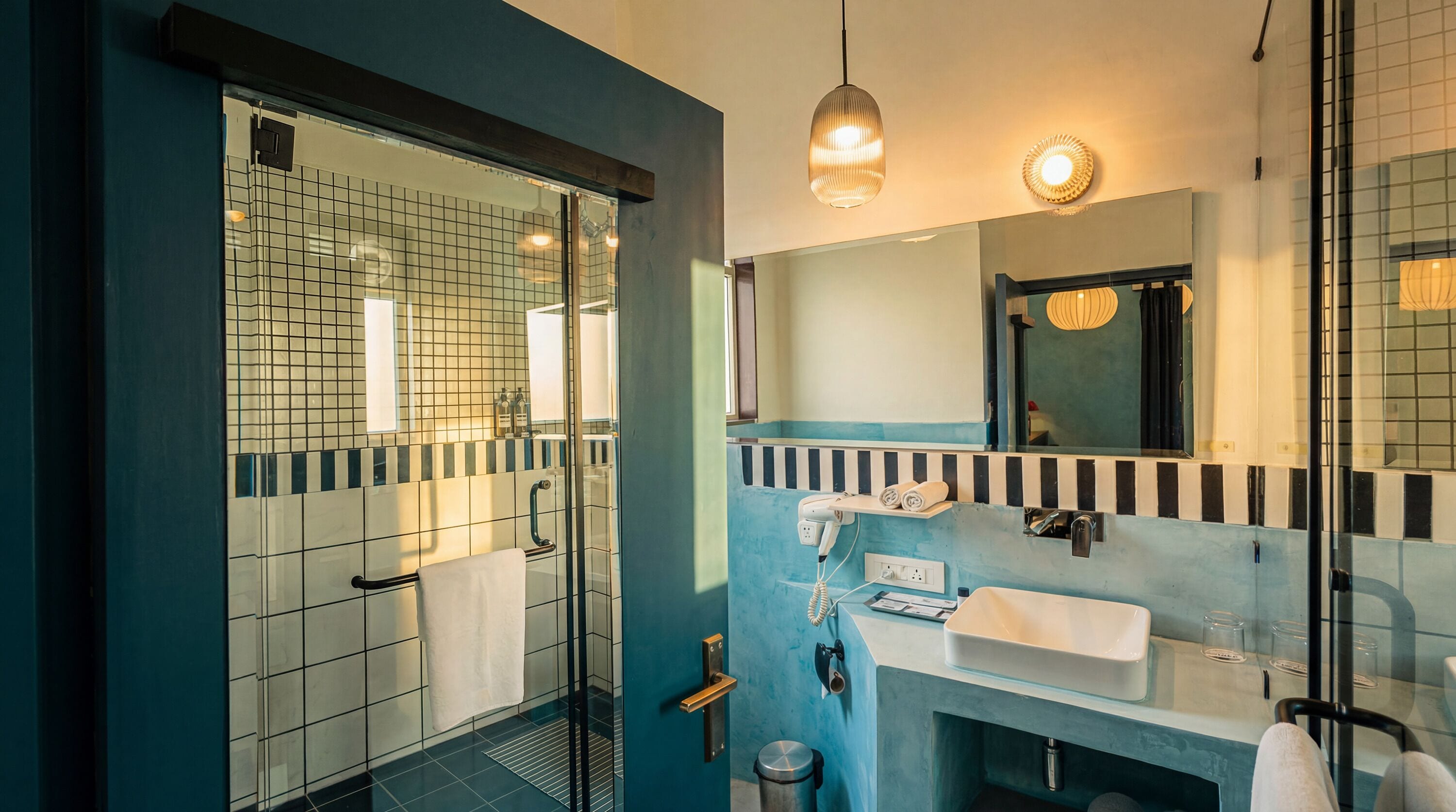 A modern bathroom with a glass shower enclosure, a sink with a towel, and a mirror with a light fixture.