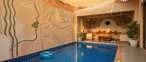 Una piscina con piastrelle azzurre, soffitto in legno e un muro con un affresco.