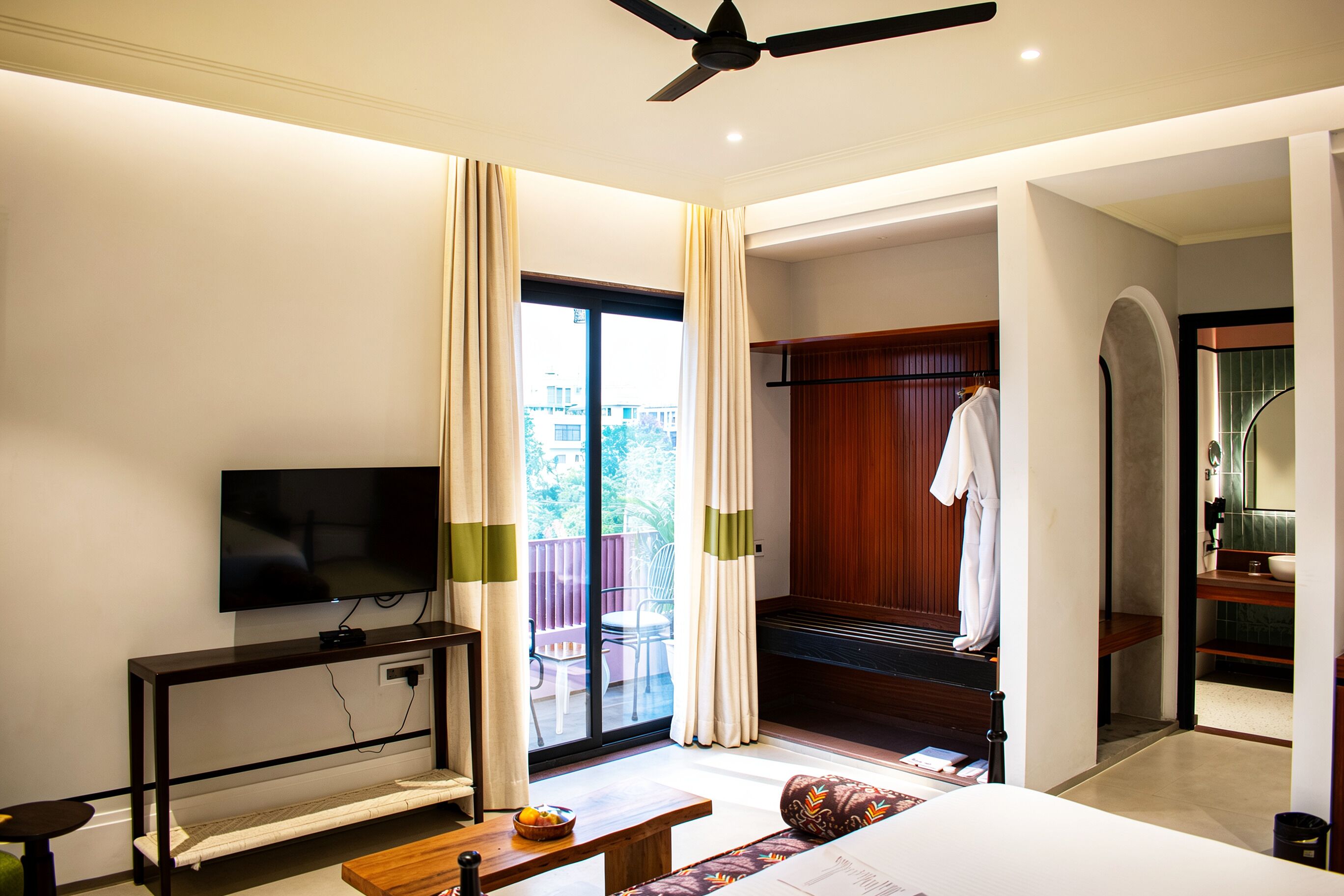 A hotel room with a television, a bed, a desk, a chair, a window with curtains, and a balcony.