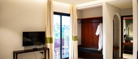A hotel room with a television, a bed, a desk, a chair, a window with curtains, and a balcony.