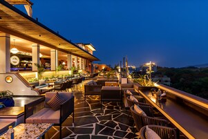 A rooftop bar with outdoor seating, a bar area, and a view of the cityscape at dusk.