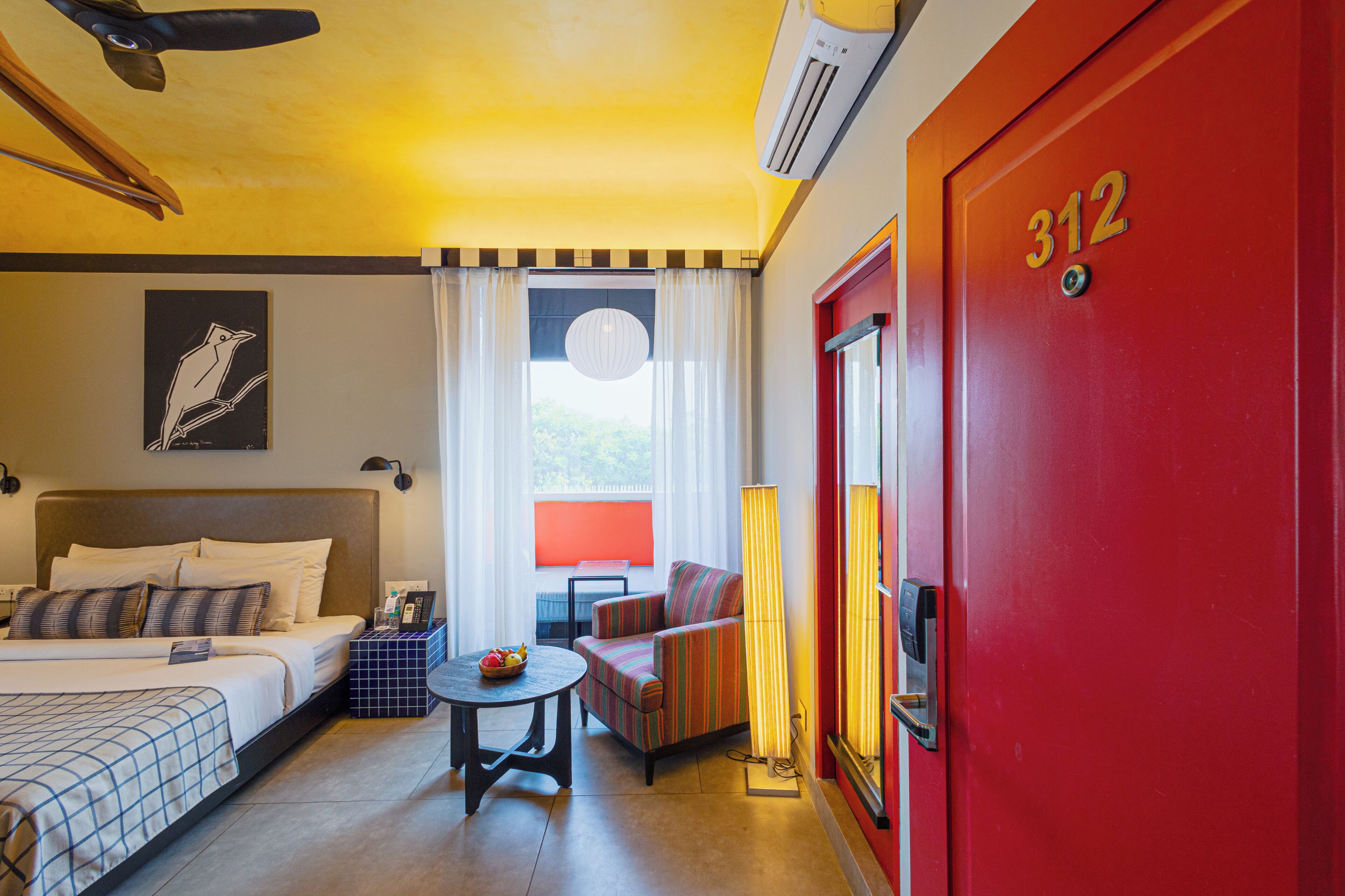 A hotel room with a bed, a sofa, a small table, and a red door with the number 312.