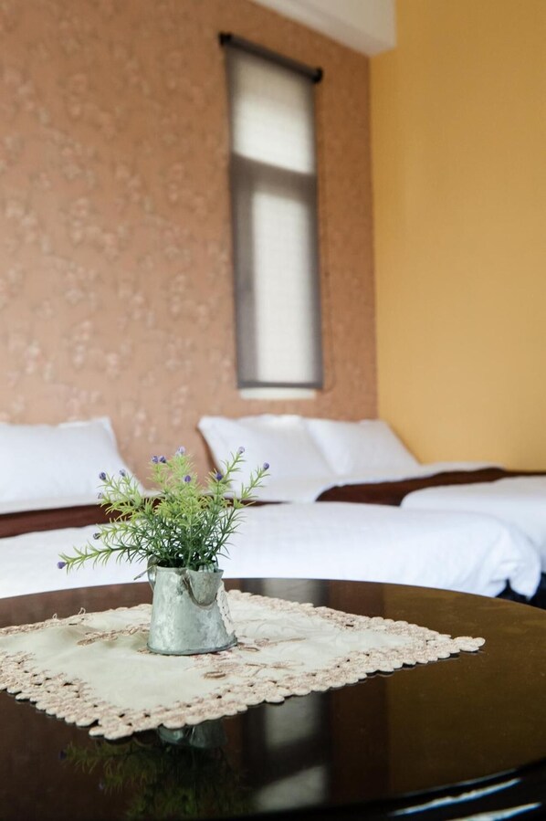 A hotel room with a bed, a bedside table with a vase of flowers, and a window with blinds. - Sea Princess B&B (Fengbin)