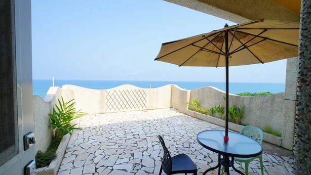 Un patio con mesa y sillas, una sombrilla y vista al mar.