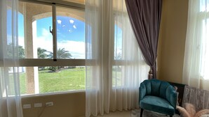 Una habitación con ventanas amplias, un sillón azul turquesa y una alfombra mullida.