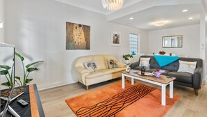 A living room with a beige sofa, a dark sofa, a coffee table, and a large orange rug. - Main Street of Goolwa - WIFI, Smart TV, Linen included (Goolwa)
