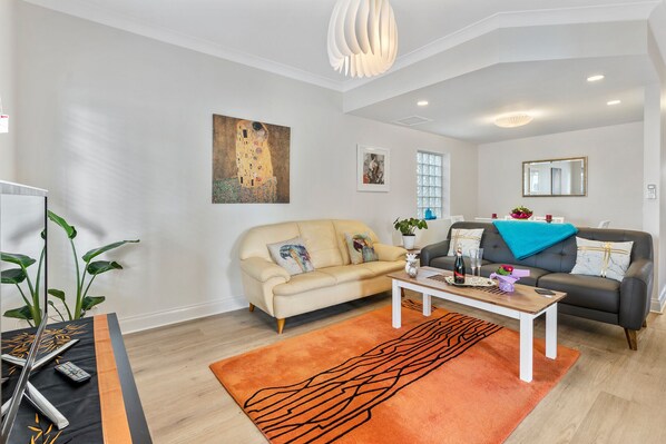Ein Wohnzimmer mit einem beigefarbenen Sofa, einem dunklen Sofa, einem Couchtisch und einem großen orangefarbenen Teppich.