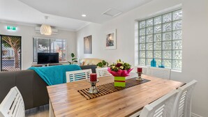 A modern living room with a wooden dining table, white chairs, a sofa, and a TV. - Main Street of Goolwa - WIFI, Smart TV, Linen included (Goolwa)